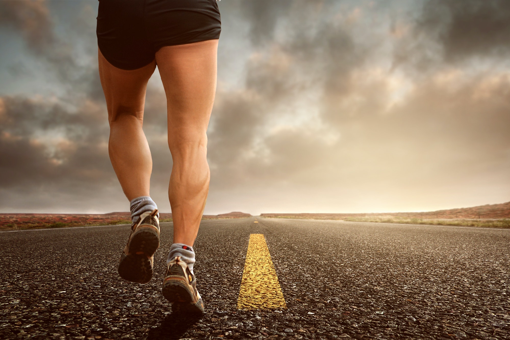 Photo of a man running showing just his lower half and legs in the middle of the road